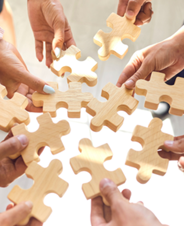 Hænder samles med puslespilsbrikker som symbol på fleksibel vagtplanlægning med blandede ansættelsestyper, hvor fuldtid, deltid og timeløn kombineres effektivt i workforce management og understøttes af præcis tidsregistrering.