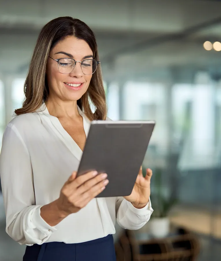 En glad forretningskvinde i en hvid bluse sidder ved sit skrivebord, taler i telefon og arbejder på sin bærbare computer. Billedet symboliserer produktivitet, kommunikation og effektiv arbejdsstyring