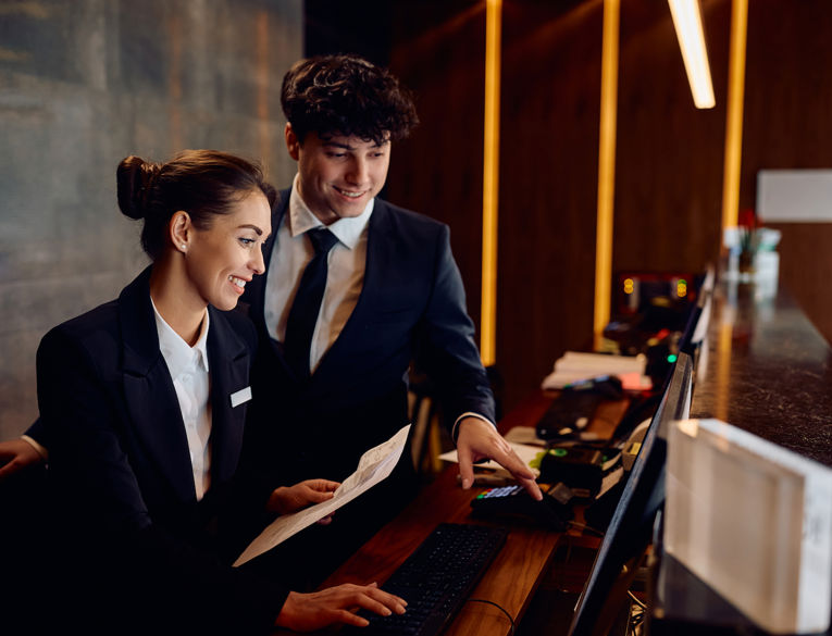 En hotelmanager og en medarbejder gennemgår gæsteserviceprocesser i receptionen.