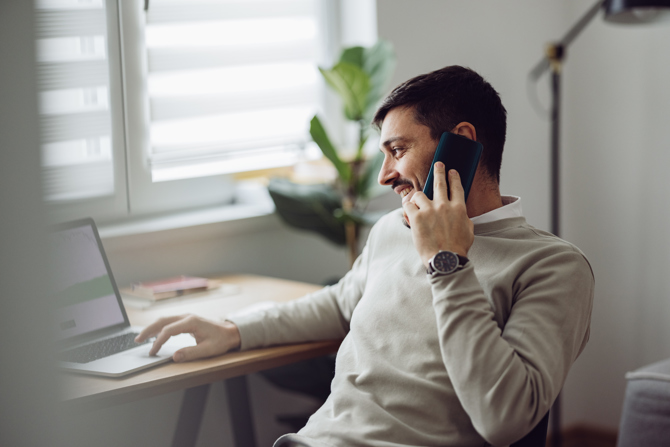 Mand arbejder hjemmefra med laptop og telefon, mens han planlægger vagter og håndterer tidsregistrering via en AI-baseret workforce management løsning.