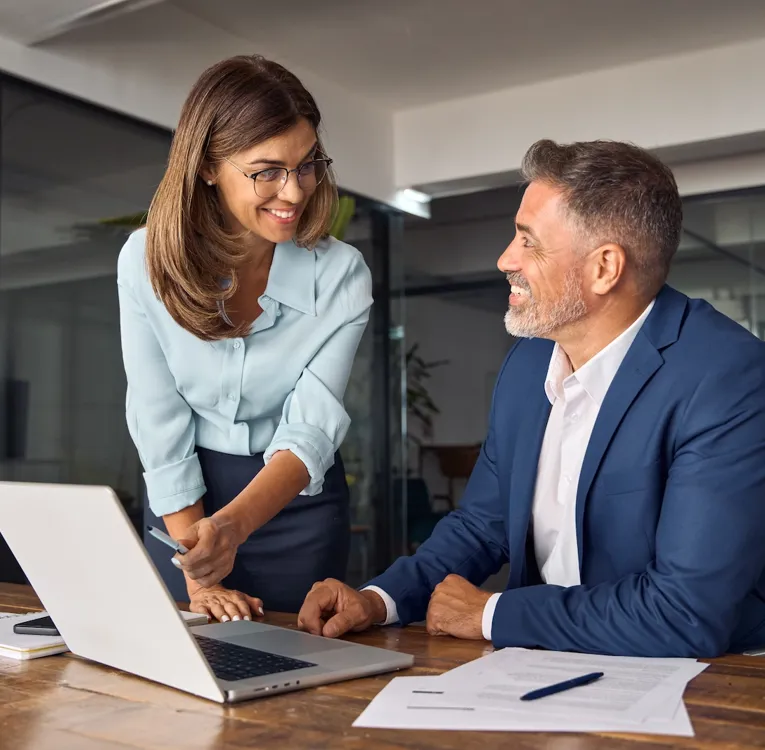 Smilende forretningsfolk samarbejder på et moderne kontor og diskuterer data på en bærbar computer. Symboliserer teamwork, lederskab og effektiv arbejdsstyring.