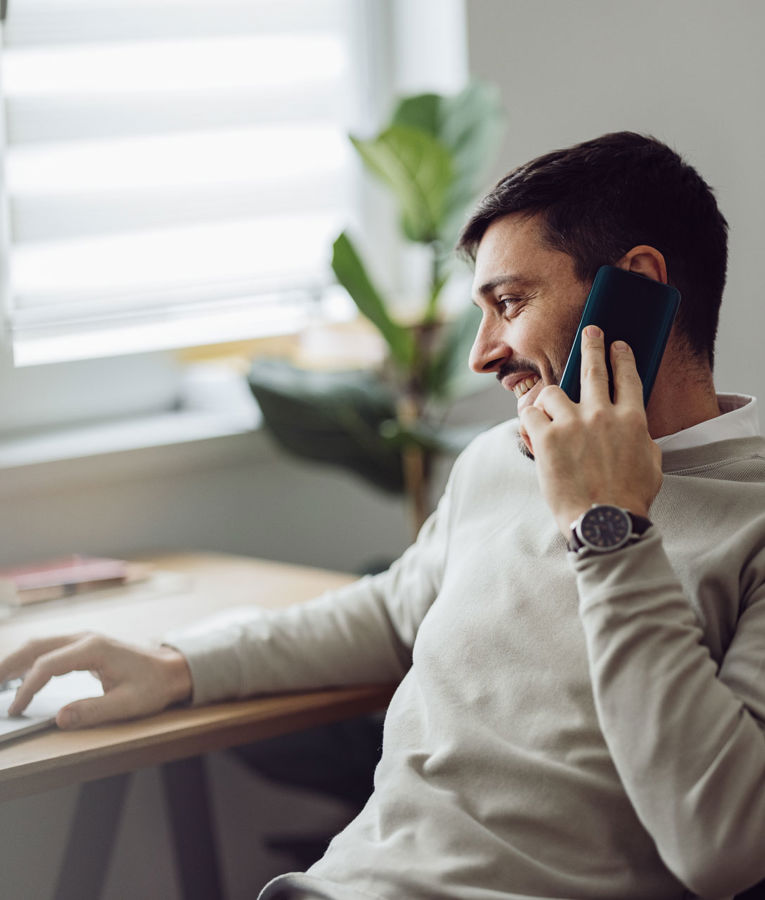 Mand arbejder hjemmefra med bærbar computer og telefon til arbejdsstyring, vagtplanlægning og tidsregistrering