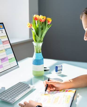 Kvinde arbejder ved computer med farvekodet vagtplan og HR-system, som illustrerer digital vagtplanlægning, bemandingsstyring og optimering af arbejdsplaner i workforce management.