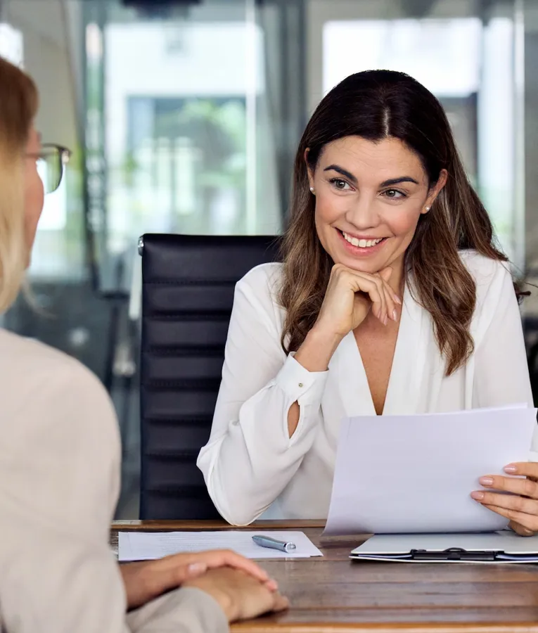 Smilende HR-manager afholder en jobsamtale i et moderne kontor, gennemgår dokumenter og engagerer sig med en kandidat. Symboliserer effektiv rekruttering og talentudvælgelse.