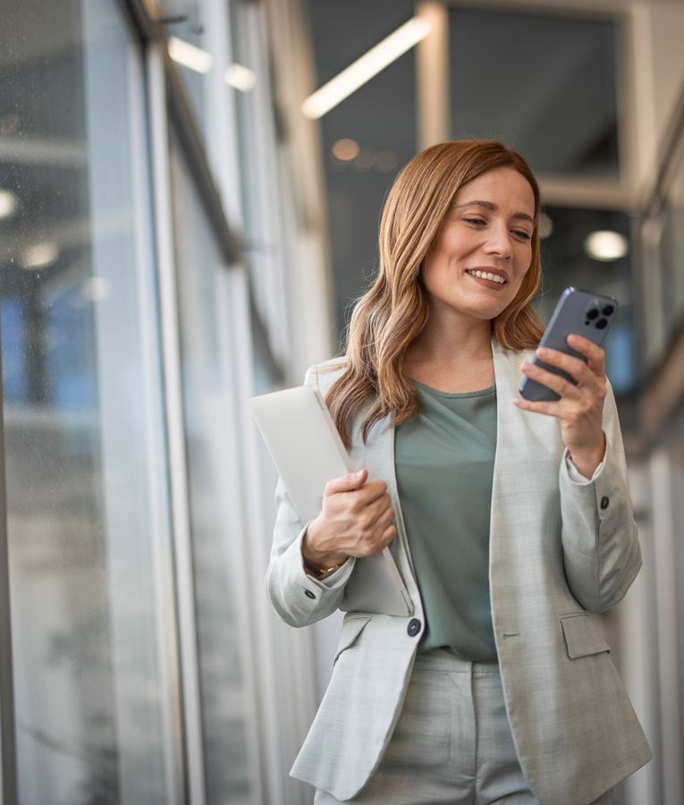 Professionel kvinde i moderne forretningsmiljø, der bruger sin smartphone til arbejdsstyring, vagtplanlægning og tidsregistrering