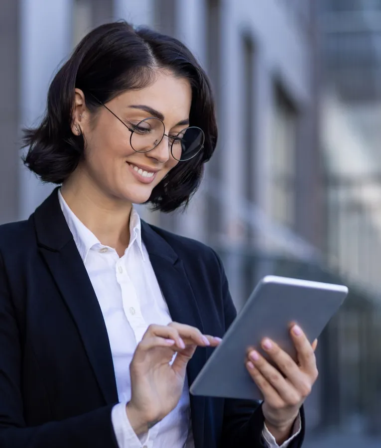 Smilende forretningskvinde bruger en tablet udendørs til at styre opgaver og arbejdsstyrkeoperationer eksternt. Symboliserer mobil arbejdsstyring og digital produktivitet.