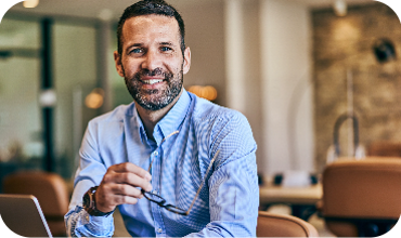 Leder med overblik smiler foran skærm – adgang til realtidsdata for tidsregistrering, bemanding og medarbejderstatus.