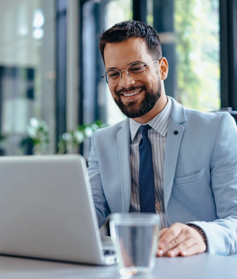Smilende forretningsmand på et moderne kontor arbejder på en bærbar computer og styrer arbejdsstyrkeoperationer og forretningsstrategier. Symboliserer digital produktivitet og lederskab.